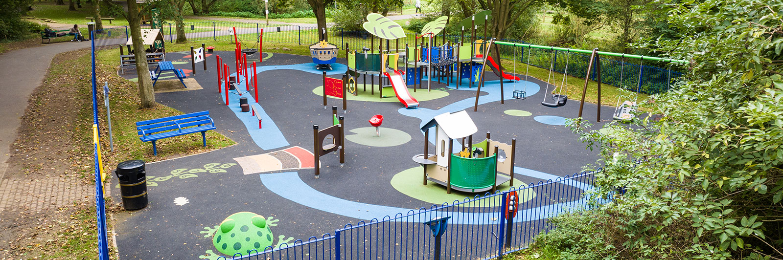 Arial shot of a large playground which is nature themed and colorful, nestled amongst trees and surrounding greenery.